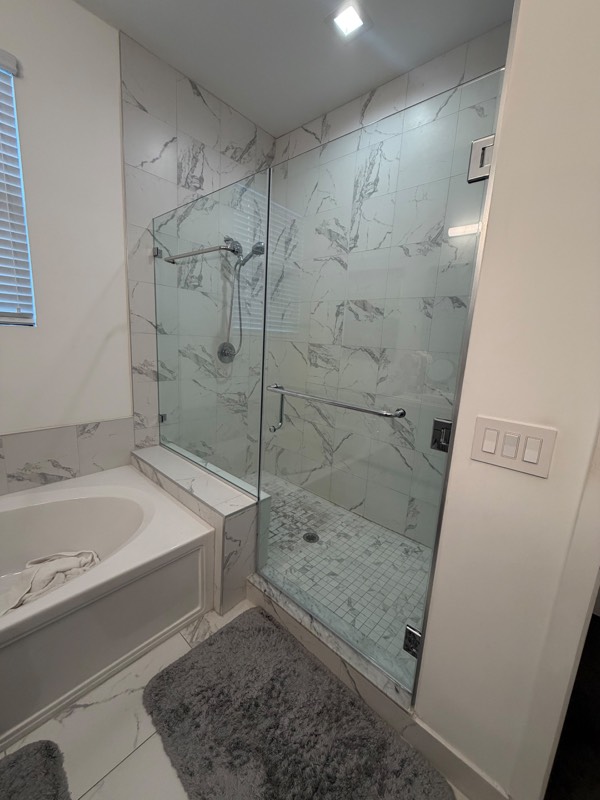 Frameless glass shower door and bench panel with chrome hardware in a white marble shower