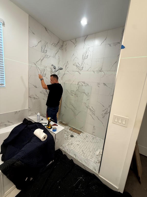 Installer checking shower walls with a laser level before setting the glass