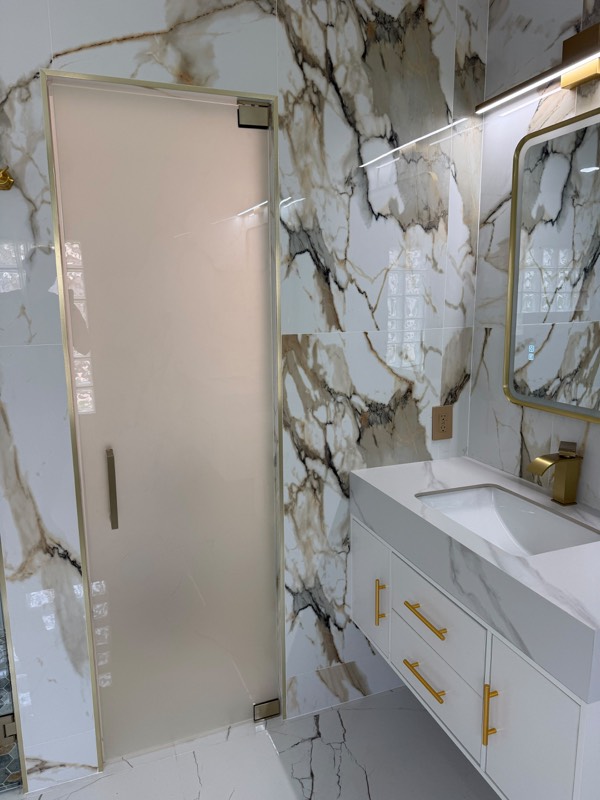 Frosted glass door with gold trim and pull handle beside a marble vanity