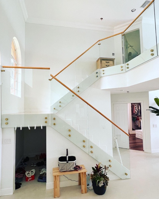 Glass stair railing with gold standoffs and a wood handrail