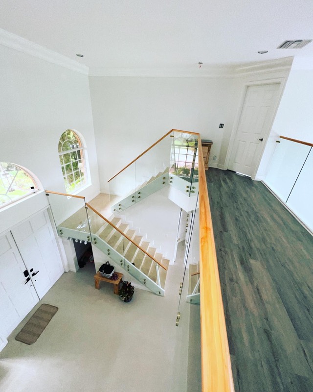 Glass staircase railing with wood handrail seen from the upper floor