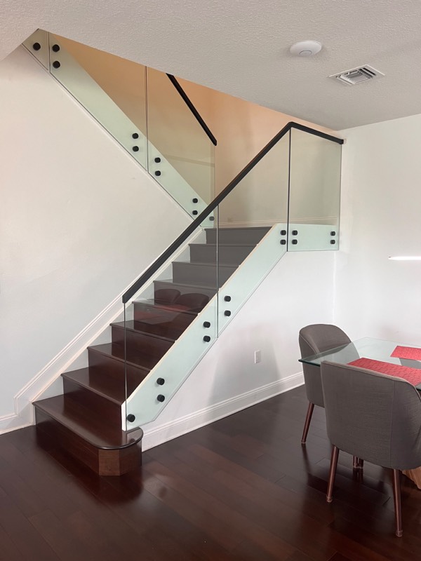 Glass stair railing with black standoffs and a black handrail on a dark wood staircase