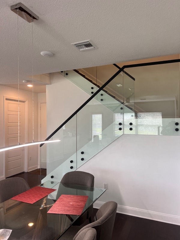 Glass stair railing seen from the dining room, with black standoff fittings