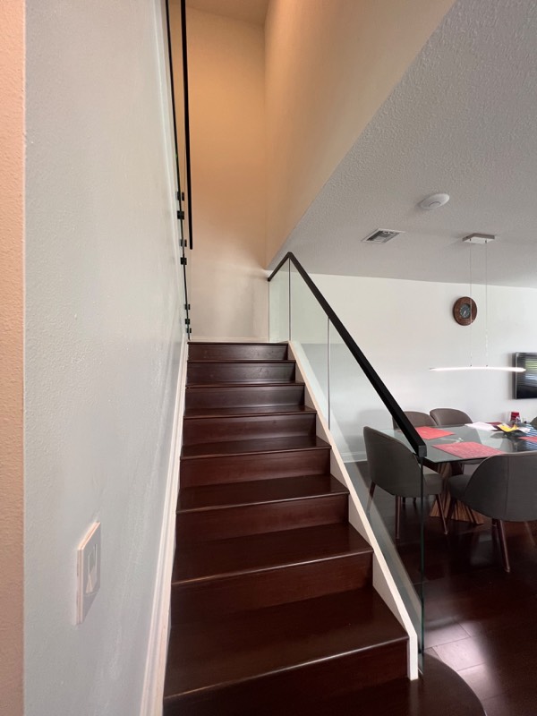 Glass stair railing with black handrail from the bottom of the stairs