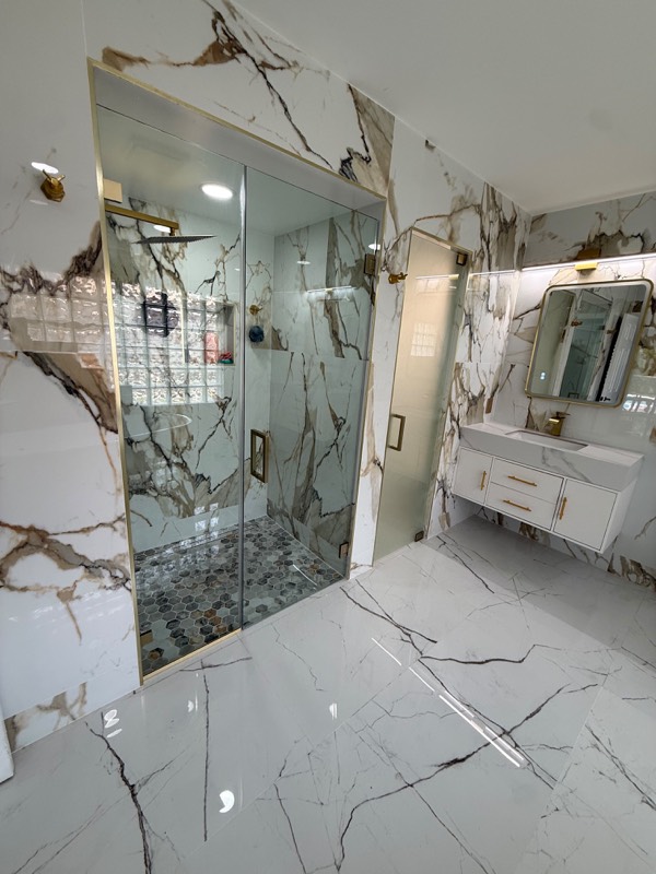 Frameless glass shower door with gold hardware and marble walls