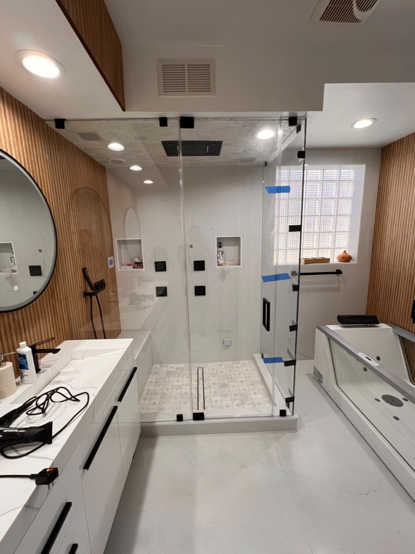 Corner steam shower enclosed in clear glass with black hinges and handle