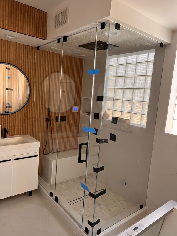 Frameless corner shower enclosure with black hardware beside a wood slat wall