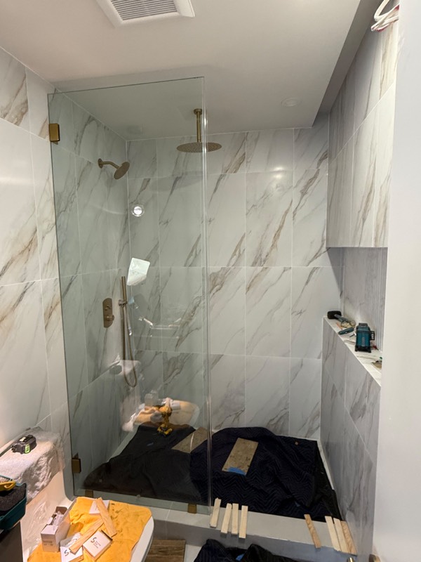 Fixed glass shower screen with gold clips in a marble tiled walk-in shower